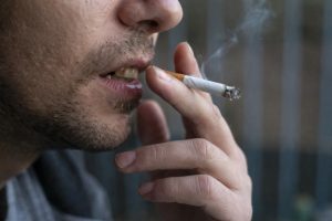Hombre esbozando ligeramente sus dientes mientras fuma